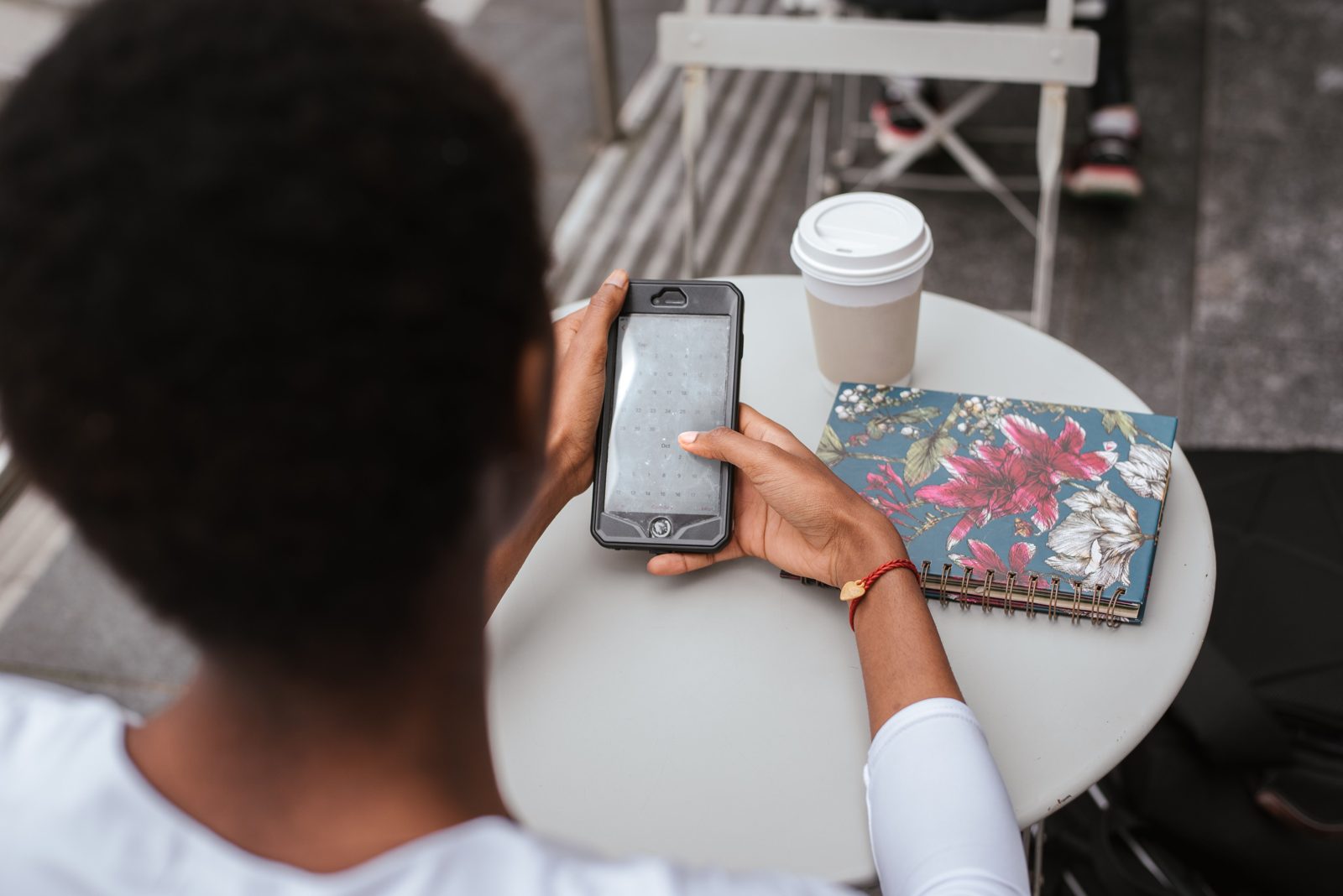 Una mujer, vista desde arriba, lee una conversación en su teléfono sentada a una mesa con un café.