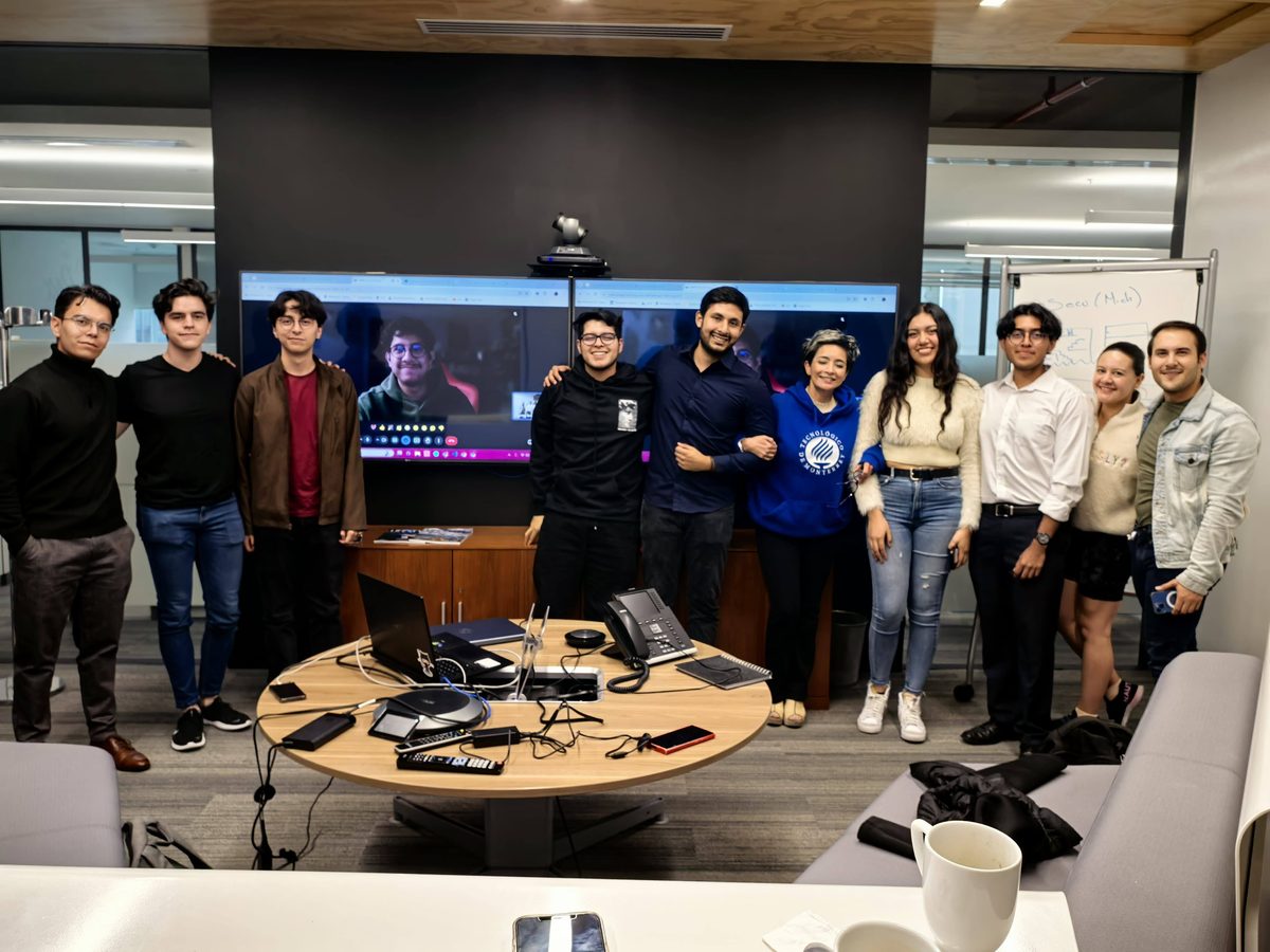 El equipo de Pernexium de pie en una sala de juntas, con un compañero conectado en la pantalla.