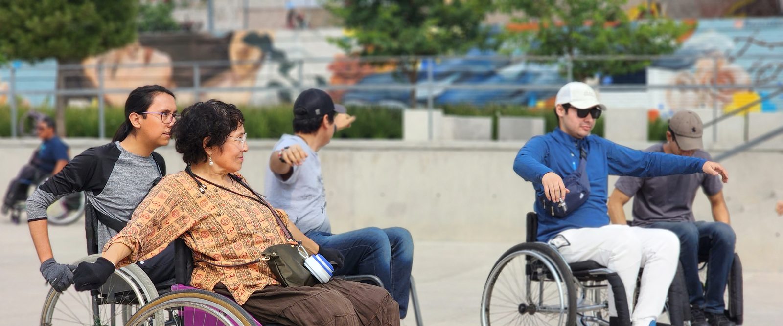 Varias personas en silla de ruedas, con brazos extendidos, durante una actividad al aire libre en una plaza.
