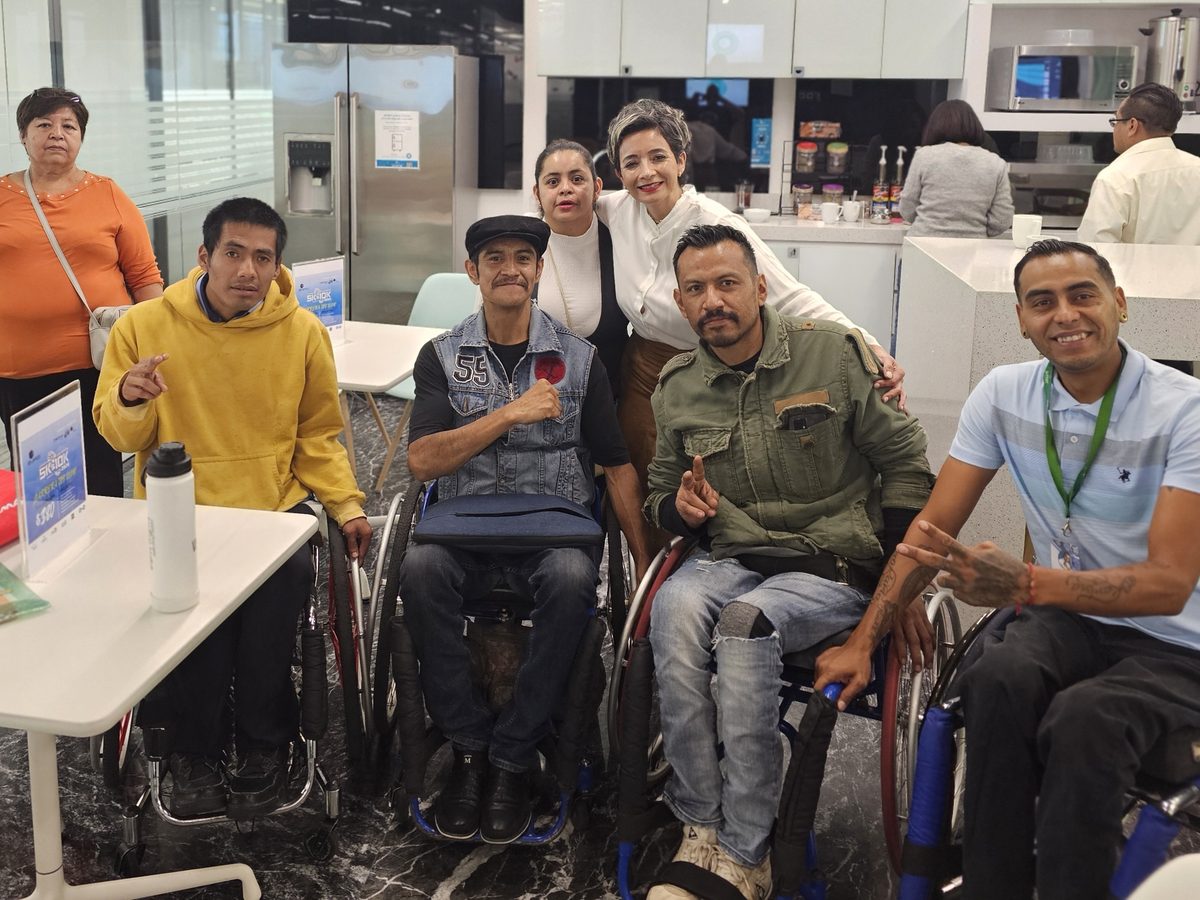 Varias personas, algunas en silla de ruedas, reunidas y sonriendo en una oficina.