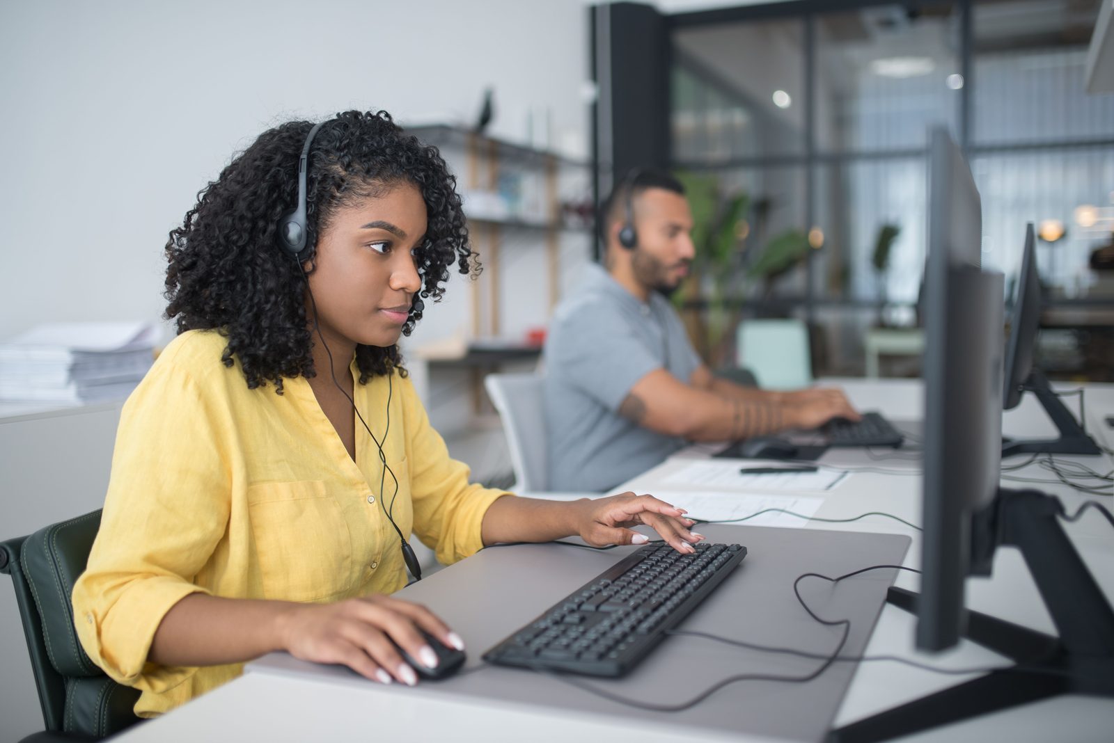 Dos agentes con diadema trabajan en sus puestos de una operación de contact center.